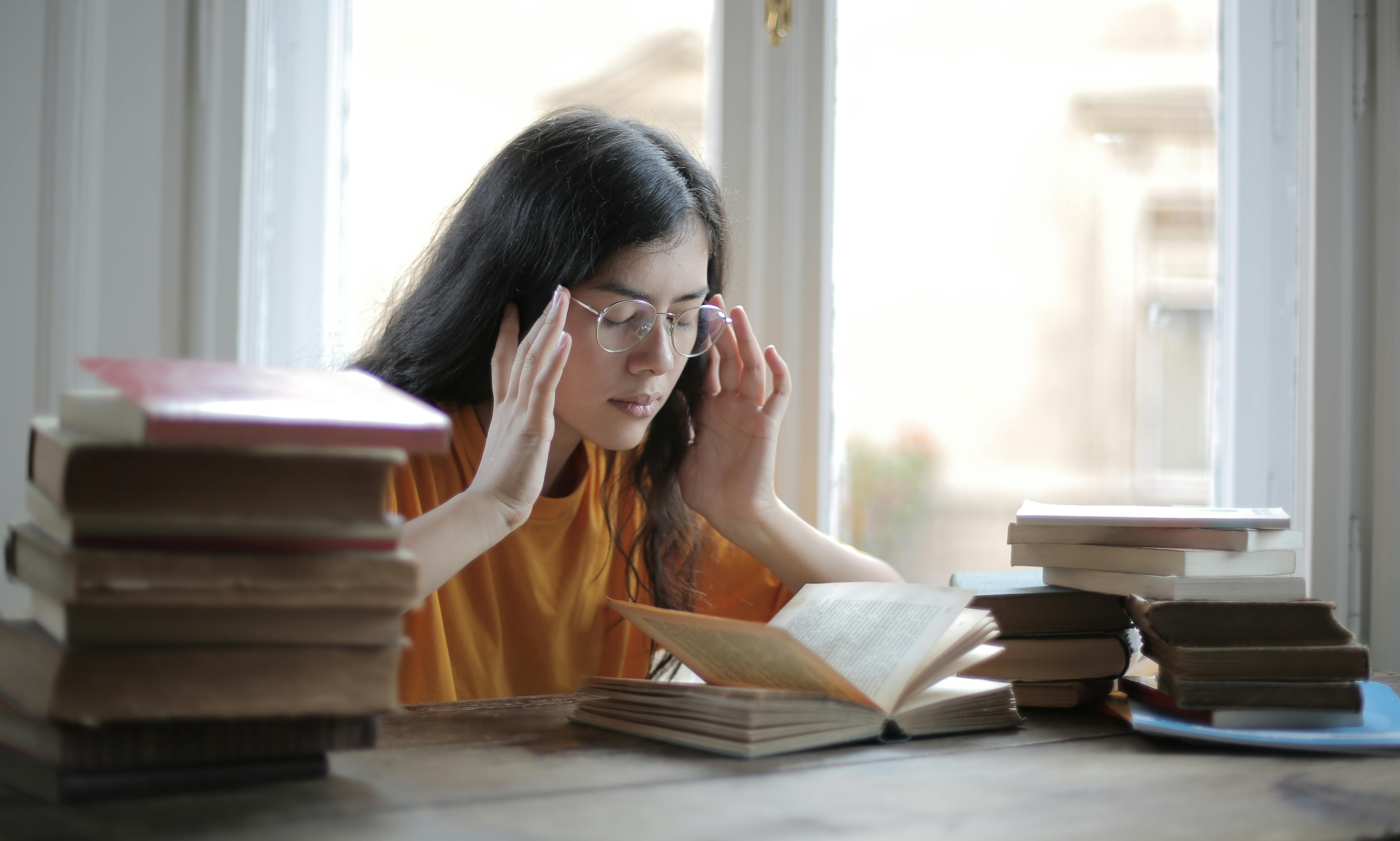 A young female student is surrounded by books and appears anxious and overwhelmed.