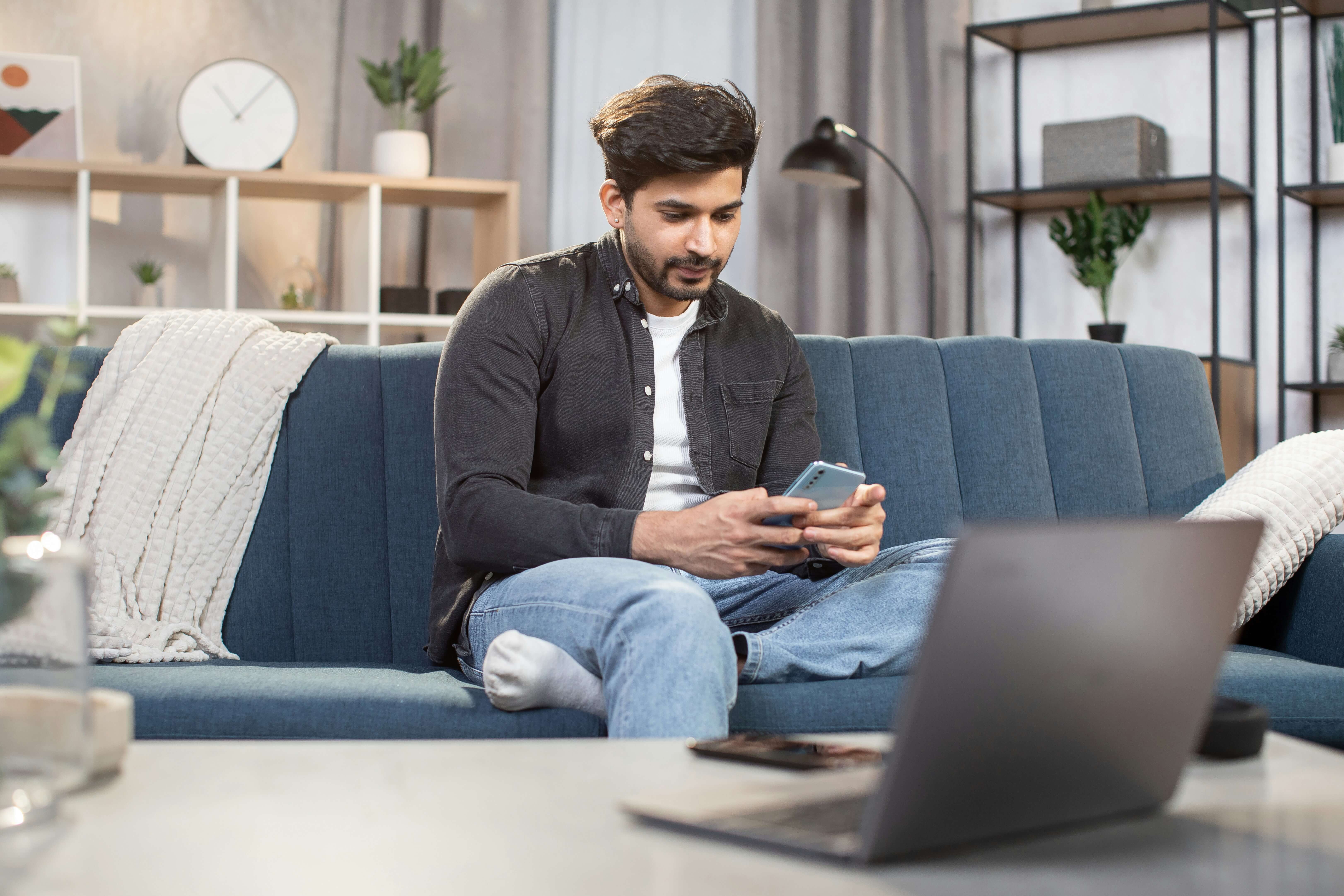 A young male computer programmer is on his phone in front of his computer