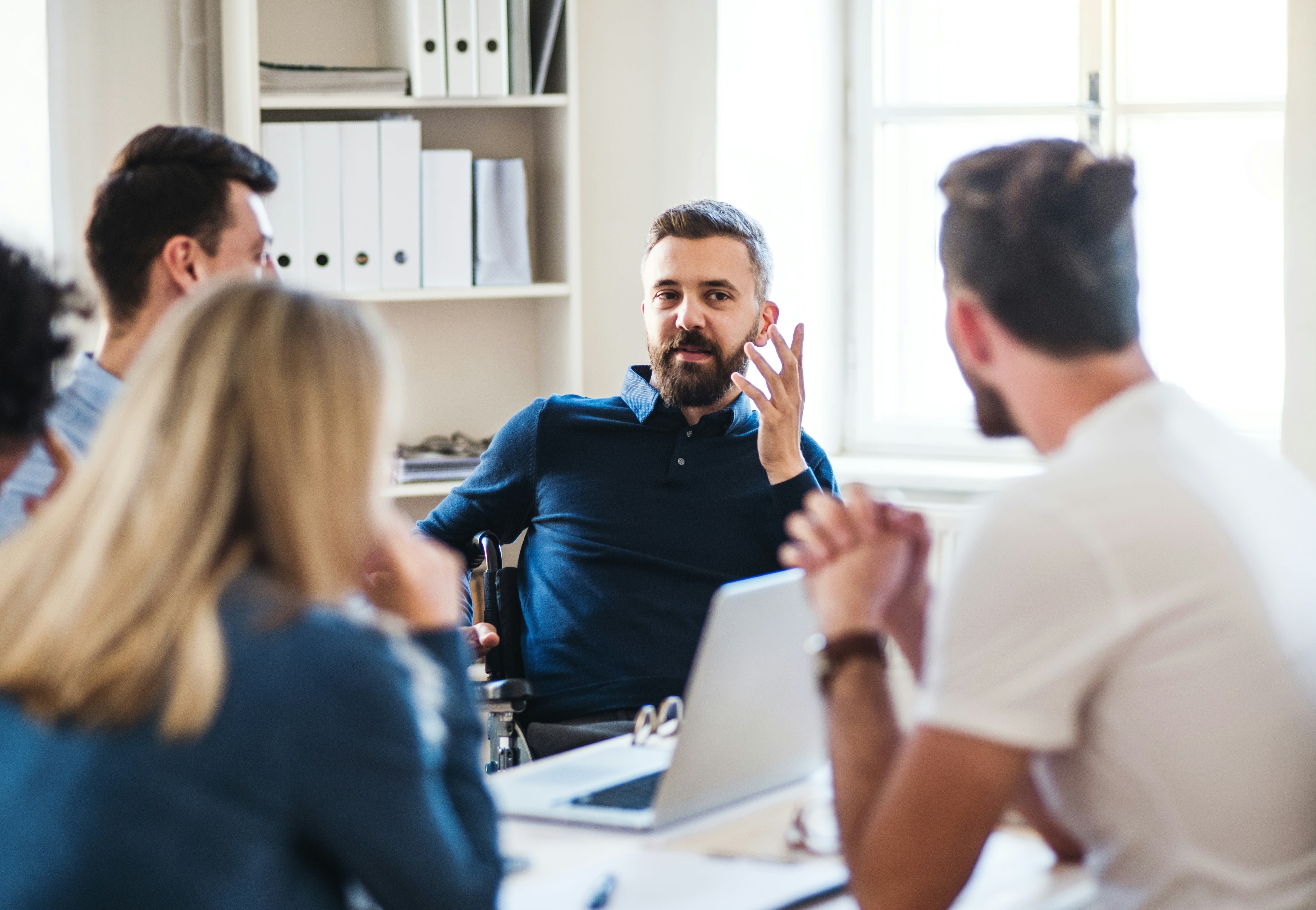 A male department head and perfectionism therapy client contributes to a team
                meeting. Staff are in a coworking space and appear engaged in the meeting.