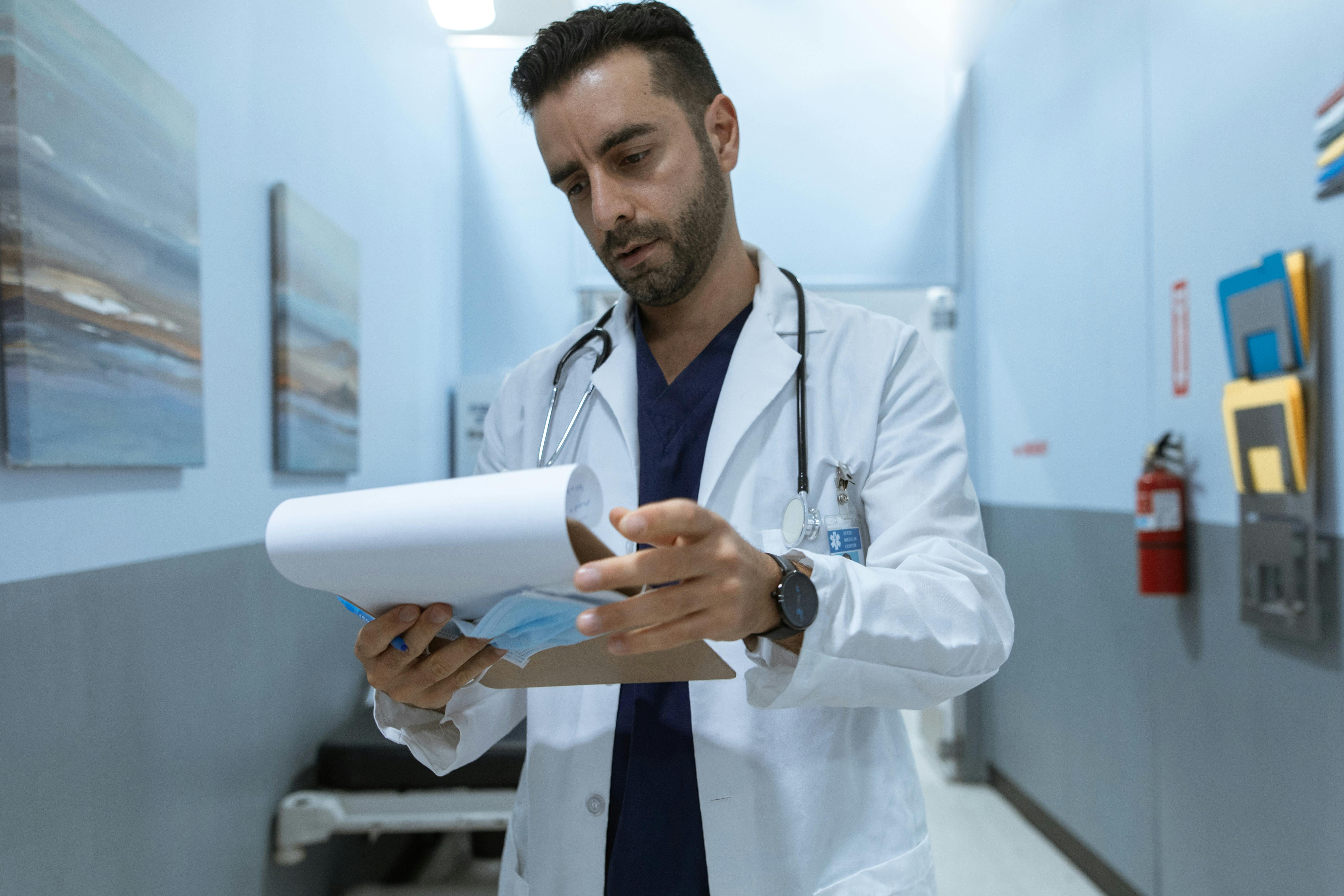 A male physician and perfectionism therapy client reviews test results while alone in a
              hospital hallway. He appears stressed and overwhelmed at work.