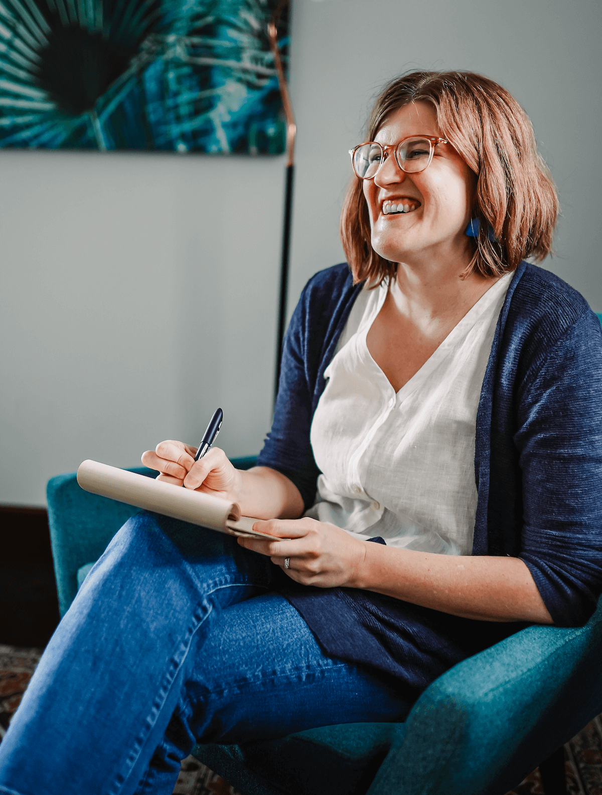 Dr. Ruth Viehoff, clinical psychologist and anxiety therapist, is shown seated and smiling while holding a notepad in her Indianapolis, IN therapy office